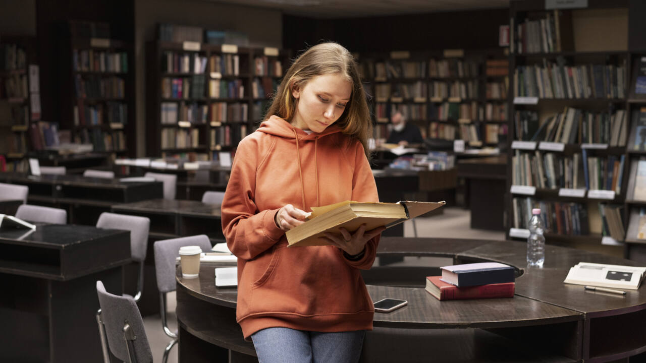 Estudante jovem lendo um livro em uma biblioteca